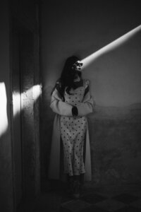 Moody black and white portrait of a woman standing in dramatic lighting, with a beam of sunlight cutting across her face.