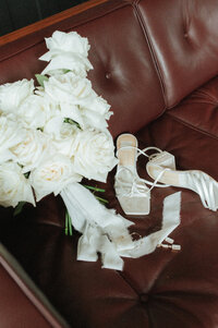Bridal details of timeless white roses and pearled pumps on a leather couch at the Surf House at the Surf Hotel in Buena Vista for her fall wedding. 