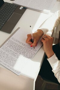 Close-up of Kaya writing in a grid notebook at a desk with a laptop.