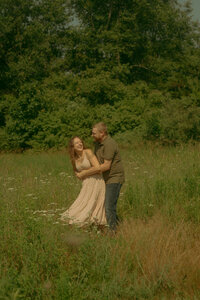 An engaged couple holds one another's faces close and giggle during an intimate moment in the sunset