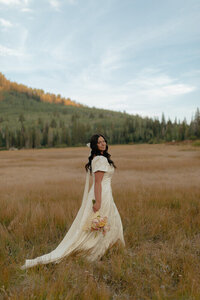 A bridal portrait of a bride in Rexburg, Idaho. She is looking over her shoulder at the camera, smiling and holding her bouquet at her side.