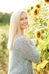 A pretty blonde girl stands among sunflowers