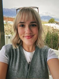 blonde woman with bangs smiling softly at the camera with glasses on her head