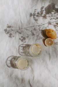 white sheet with floral shadows, whole lemon and half cut lemon, glass of water with lemon slices