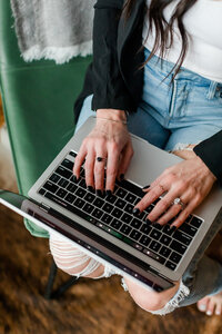 Close-up of Allie Clark typing on a MacBook Pro, highlighting the detailed, hands-on nature of design work at Allie Clark Designs.