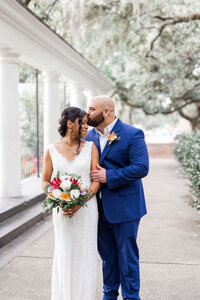 Bride and groom holding hands in front of a textured wall with ivy and a wrought iron balcony in Savannah's historic district during their elopement.