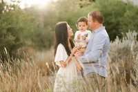 Mom, Dad and little boy snuggle in golden glowing light.