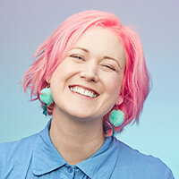 Smiling woman with pink hair against blue green gradient.