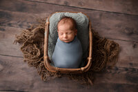 newborn baby boy wrapped in dusty blue wrap in basket at his Detroit Newborn photography session