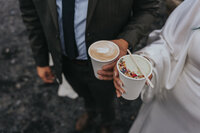 Newlyweds hold coffees in their hands on the Black Sand Beach of Iceland