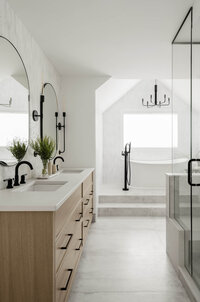 Bright, airy ensuite bathroom featuring white oak cabinetry, floor-to-ceiling tiled walls, and sleek black fixtures for modern contrast.
