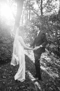 Bride and groom holding hands in the forest at sunset.