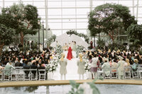 Hindu bride in red lehenga walking down the aisle toward the mandap during a traditional Indian wedding ceremony, photographed with soft natural light.