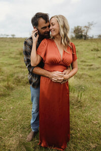 A couple embraces in a field with an overcast sky. 