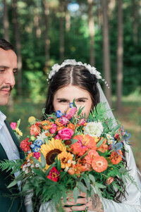 A newlywed couple standing close with a bouquet covering one of their faces