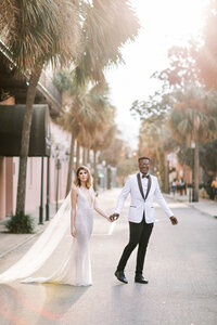 Wedding Photo of interracial couple holding hands in wedding gown and tuxedo on streets of Charleston, South Carolina