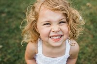 A joyful young child with curly hair smiling outdoors during a family photography packages session.
