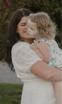 Brigette is holding her daughter Isabella outside.