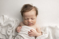 sleeping newborn baby wearing headband posed in basket with white  blanket