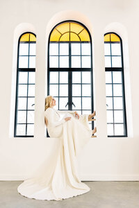 Bridal photos of a bride sitting in a windowsill while showcasing the entire window