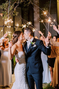 Bride and groom kiss after walking through sparklers leaving their wedding reception