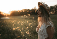 woman looking into the sun in a field with dandelions blowing past.