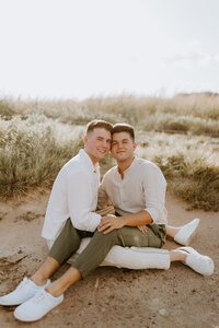 Two men sitting on the ground while smiling and embracing