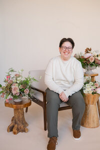 Amy sitting on a chair smiling with flowers on either side