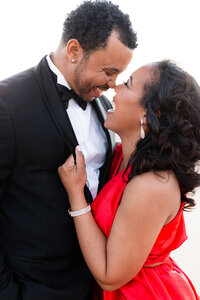 Couple laughing together in red dress and tux during engagement session