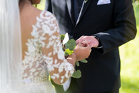 Bride in lace sleeved wedding dress slides wedding ring onto her husband's finger