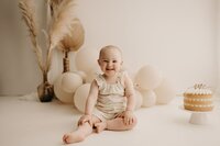 Happy one-year-old during a cake smash photoshoot with 'one' topper in Mullingar, Ireland.