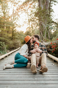 Sweet moment of parents kissing with their happy baby smiling during a Charlotte family photography session.
