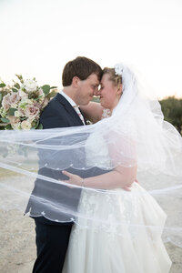 A bride and groom sharing a heartfelt kiss under a veil on a scenic dirt road, captured beautifully by an Austin wedding photographer.