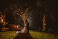 The bride and groom pose with their bridesmaids, capturing a joyful moment as the sun sets in the background.