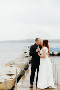 bride and groom kissing on a boat dock while it was raining with row boats lining the dock