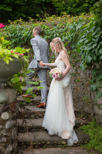 Groom holds bride's hand and leads her up fairytale garden steps