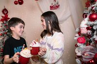 Brother and sister in Christmas jumpers sharing cocoa in Calini Weddings Studio – cheerful holiday portrait with twinkling lights and decorations.