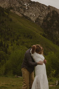 A husband holding hands with his pregnant wife, walking in a grass field outside.