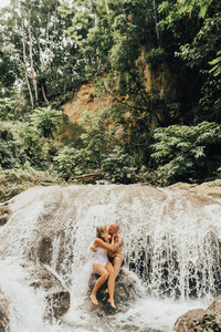 couple kissing on a rock underneath a waterfall