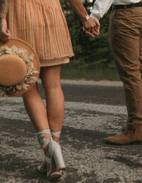 Couple holding hands with a view of the woman's hat and holding her hands.