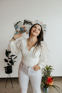 Taysha facing the camera wearing an all white outfit with plants and a brand moodboard behind her.