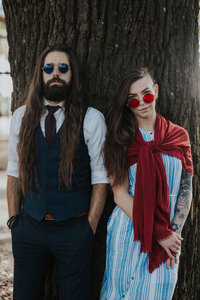 couple in glasses lean on tree