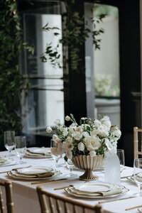 A detail photo of a wedding tablescape. A white rose floral arrangement is the focal point, while ivy cascades in the background.