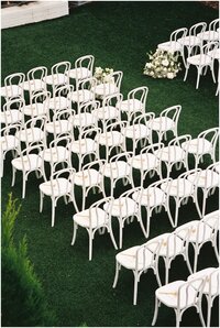 A details image looking down at white wooden chairs set up in a lawn for a wedding ceremony