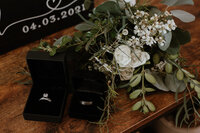 two ring boxes with rings on table next to flowers