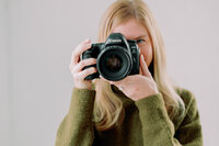 Nikki holds a camera while smiling.