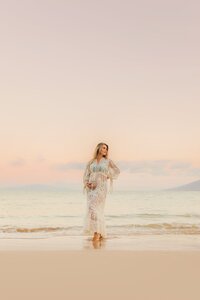 pregnant woman in pink maternity gown kisses her husband at sunrise in maui