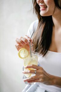 A person is holding a glass with a refreshing drink, garnished with a slice of lemon.