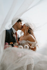 Bride and groom kissing under veil