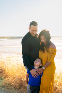 Sweet moment of a family embracing in a sunlit field with their child looking up lovingly, captured by Ellobelle Photography Family Photographer